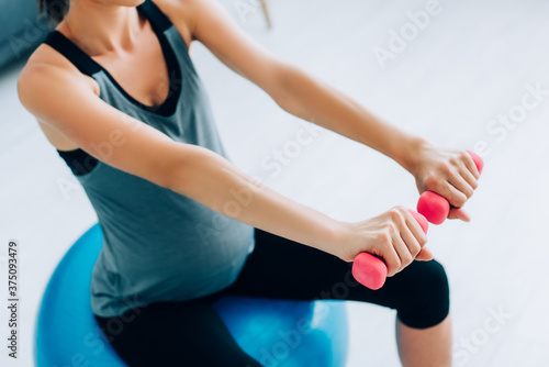 Cropped view of pregnant woman in sportswear exercising with dumbbells and fitness ball