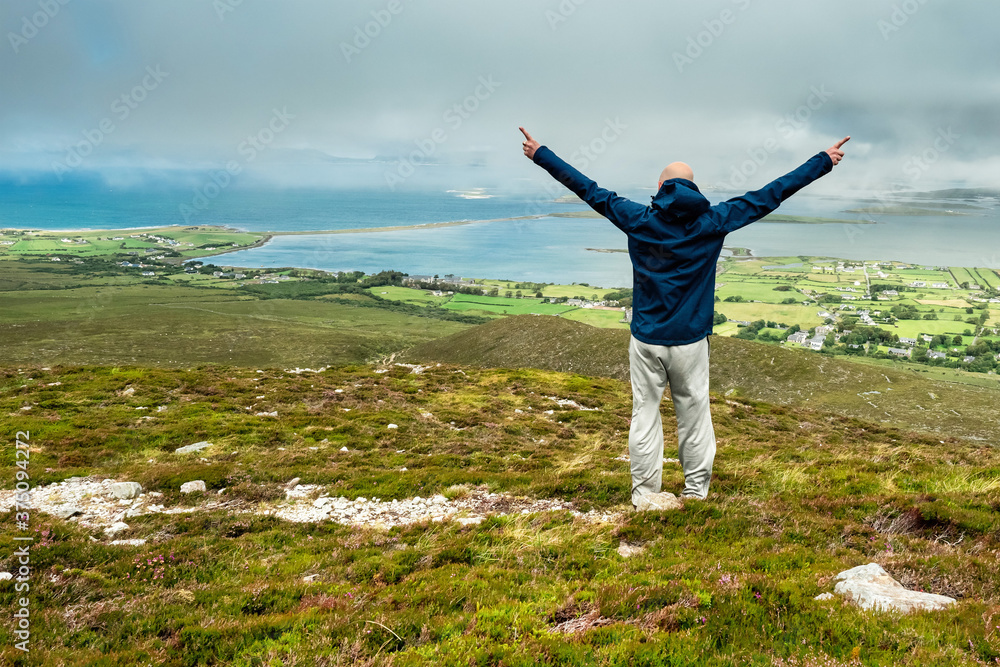 Man enjoying view on Clew Bay from Croagh Patrick, Westport, county Mayo, Ireland. Blue cloudy sky, Hand in the air. Man enjoying view on Clew Bay from Croagh Patrick, Westport, county Mayo, Ireland. Blue cloudy sky, Hand in the air.