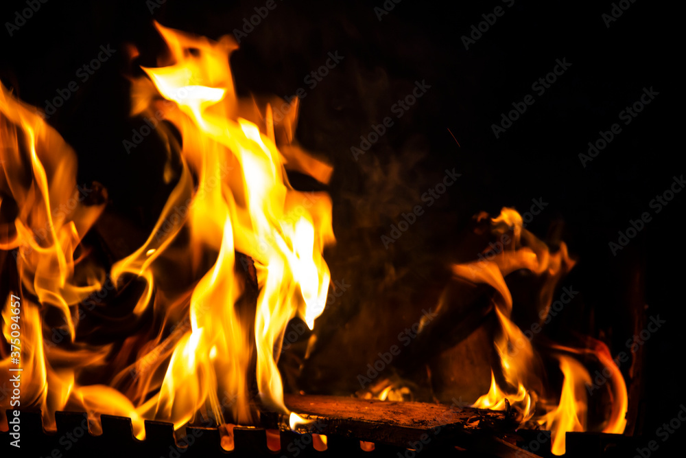 Fire on a dark background. Fire from firewood close up. Flaming burning sparks close-up, fire patterns. Red and orange Infernal glow of fire in the dark. Fire on a dark background. Fire from firewood close up. Flaming burning sparks close-up, fire patterns. Red and orange Infernal glow of fire in the dark.