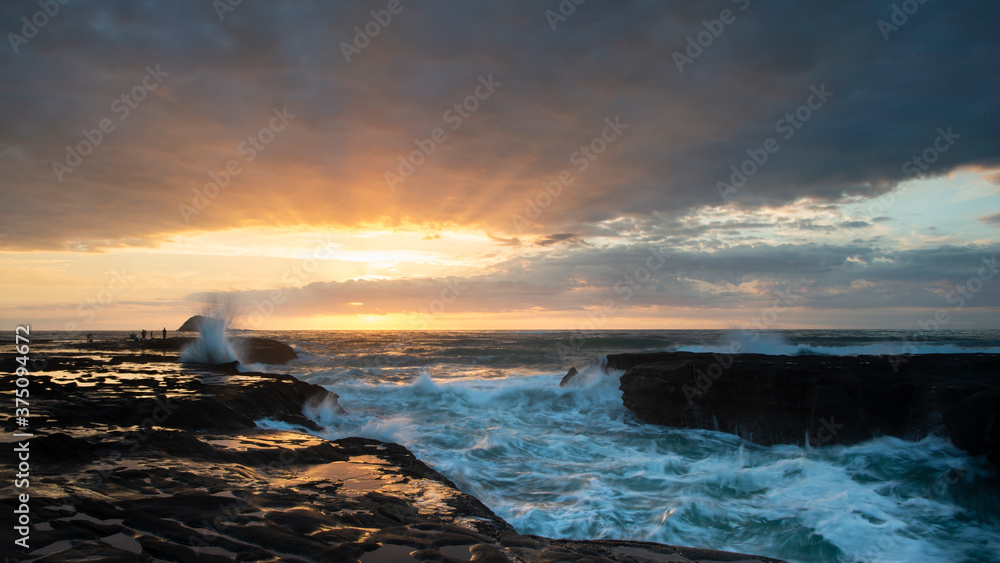 Fototapeta premium Sunset at Muriwai beach with splashing waves against the rocks