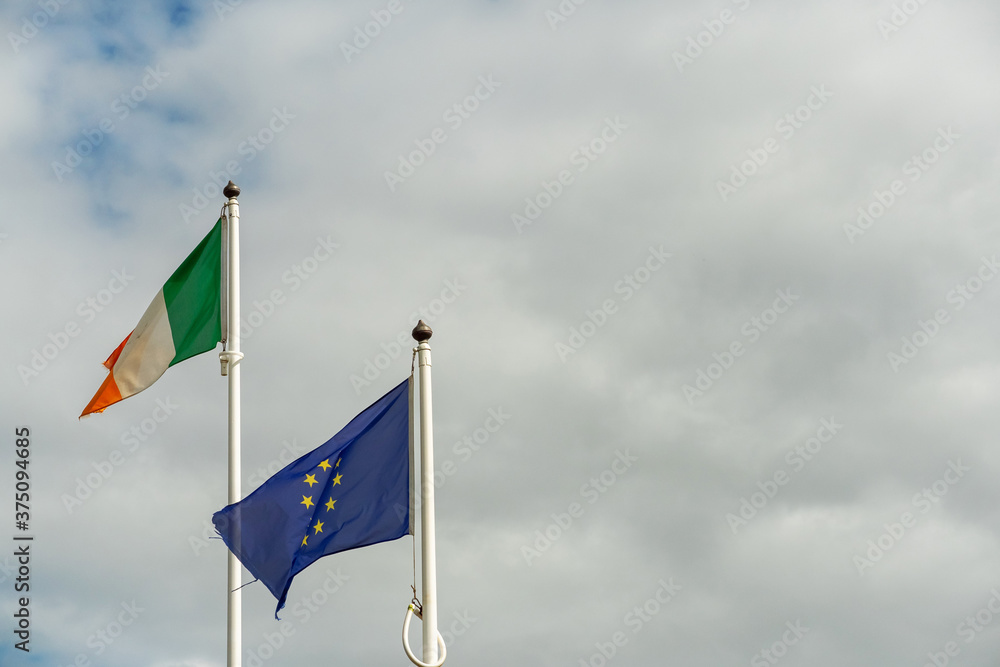 National flag of Ireland and Euro Union flag against cloudy sky background.