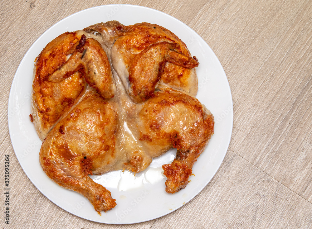 Roasted tobacco chicken on a white plate on a wooden table. Roasted tobacco chicken on a white plate on a wooden table.
