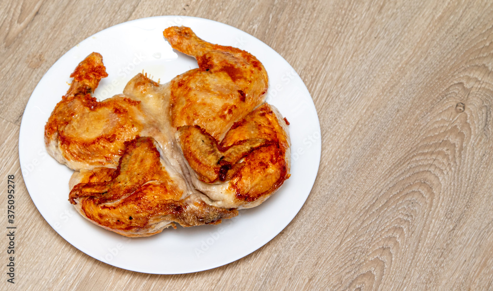 Roasted tobacco chicken on a white plate on a wooden table. Roasted tobacco chicken on a white plate on a wooden table.