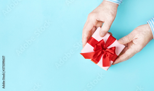 Gift box with red bow in male hands on pastel blue background. Top view. Copy space