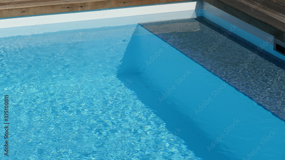 Schöner blauer Pool mit einer Umrandung aus Holz und einer kleinen Bank für die Füße im Wasser