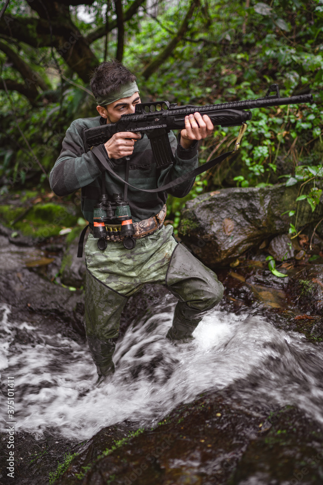 Soldier or revolutionary member or hunter in camouflage in the stream aiming the gun in his hand, hunter concept
