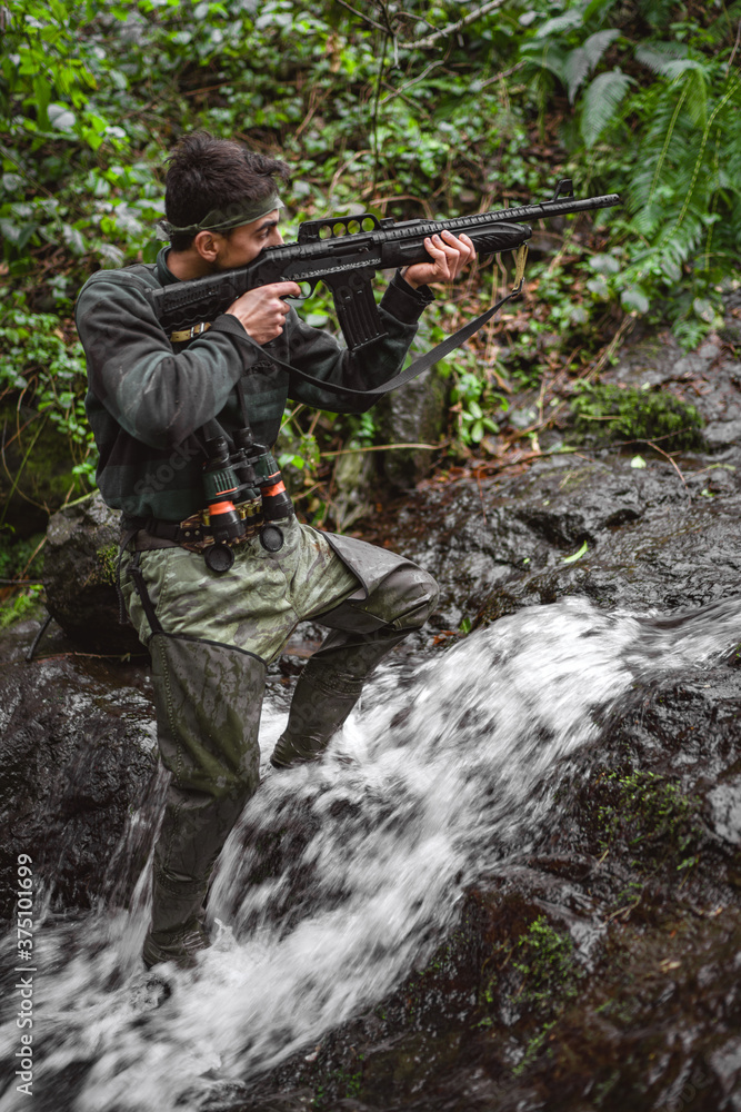 Soldier or revolutionary member or hunter in camouflage in the stream aiming the gun in his hand, hunter concept
