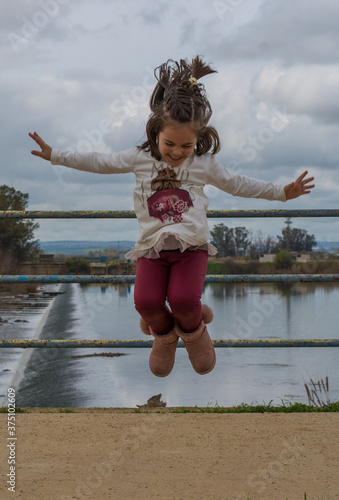 Girl jumping in the field. Stock photo of a young toddler girl jumping in the air in the field. She is looking at the camera and smiling. © Nanci