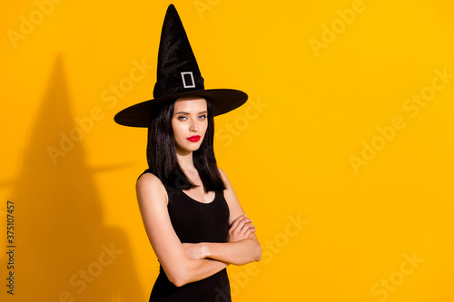 Profile photo of cute lovely young sorceress lady crossed arms serious look prepare evil potion destroy world wear black headwear dress isolated bright yellow color background