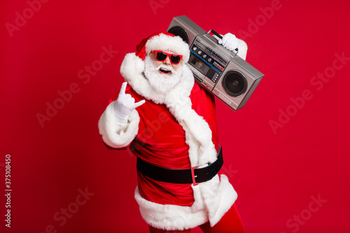 Full body size photo of retired old man grey beard hold boombox show horns make youngsters envious hard loud noise wear santa costume sunglass headwear x-mas isolated red color background