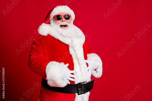 Photo of retired old man grey beard hands big belly laughing out loud kid tell great christmas joke wear santa costume gloves coat sunglass headwear isolated red color background