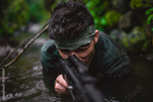 Soldier or revolutionary member or hunter aiming with gun in his hand in camouflage in the river, hunt concept