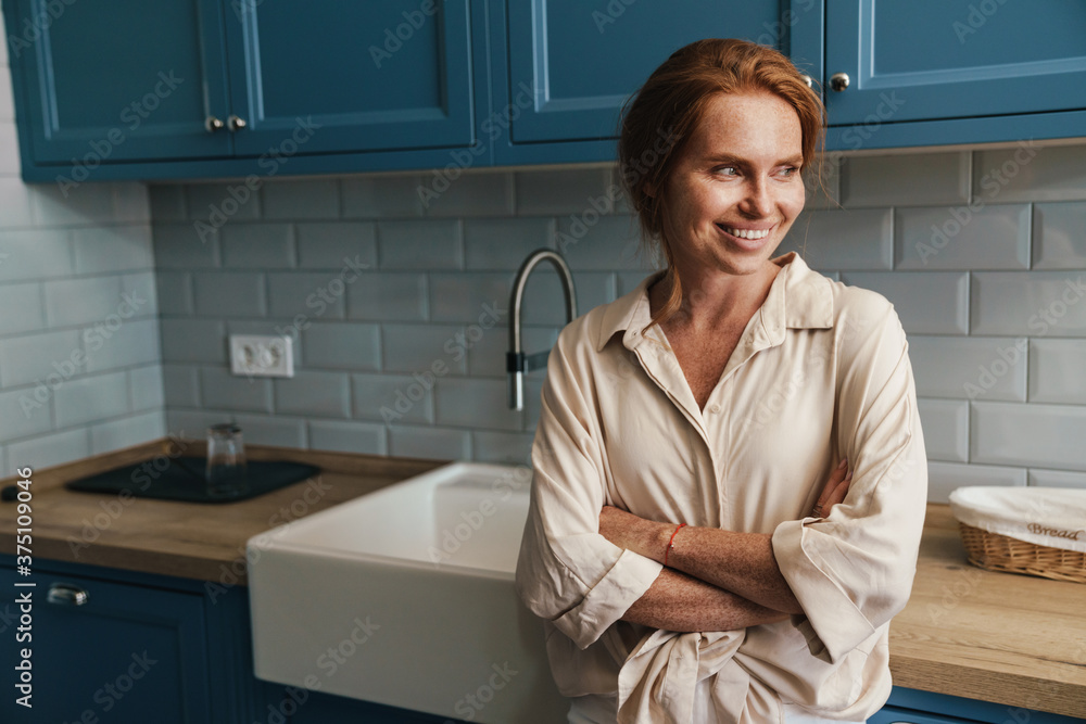 Image of happy redhead woman smiling and looking aside while standing Image of happy redhead woman smiling and looking aside while standing