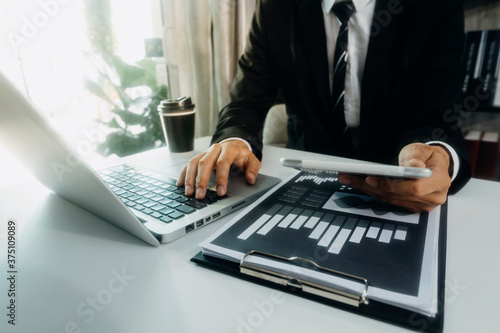 Businessman hands working with finances about cost and and laptop with tablet, smartphone at office in morning light