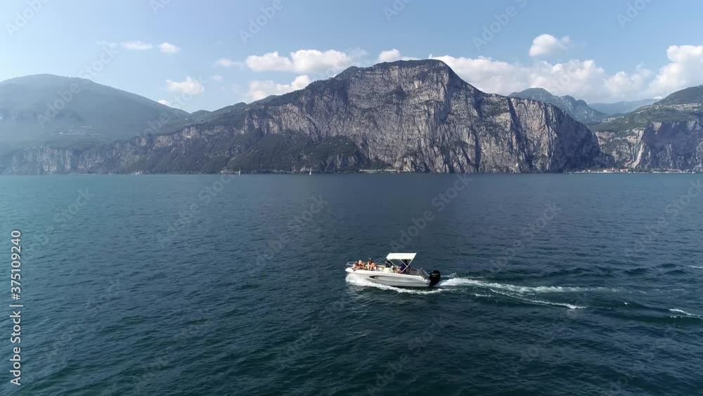 Low altitude aerial view of motorboat with sun tanning family onboard small boat moving over quiet lake in far background showing mountainous scenery which also is the coastline 4k high resolution Low altitude aerial view of motorboat with sun tanning family onboard small boat moving over quiet lake in far background showing mountainous scenery which also is the coastline 4k high resolution