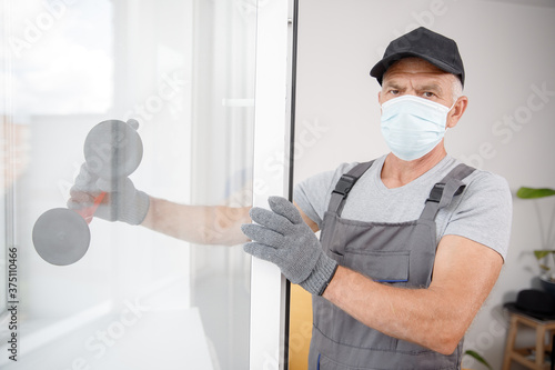 Obraz na płótnie Worker man in medical mask installs plastic upvc windows and doors white with va