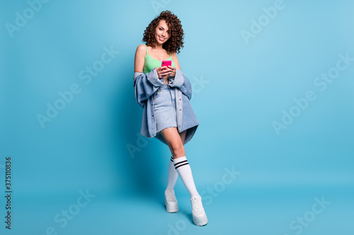 Full body photo of positive girl use smart phone enjoy social network communication wear stylish green crop top sneakers isolated over blue color background