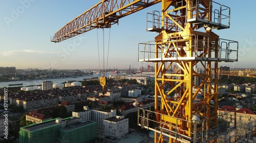 Drone point of view moving up around crane tower in construction site sunset. Close up view of the crane tower lifting material in building site. Industry construction concept footage Shanghai China