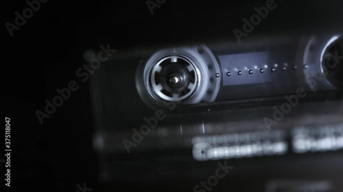 An audio cassette spools tape in extreme macro. Shallow depth of field with focus on the rorating spool. Suggests an interrogation or phonetap. 