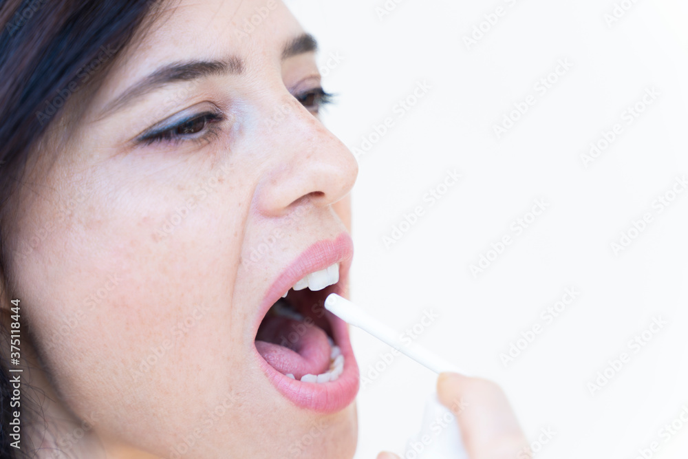 Obraz premium Spray for sore throat. Photo of a woman who treats her throat with a spray and sprinkles it in her mouth. The concept of health and disease.