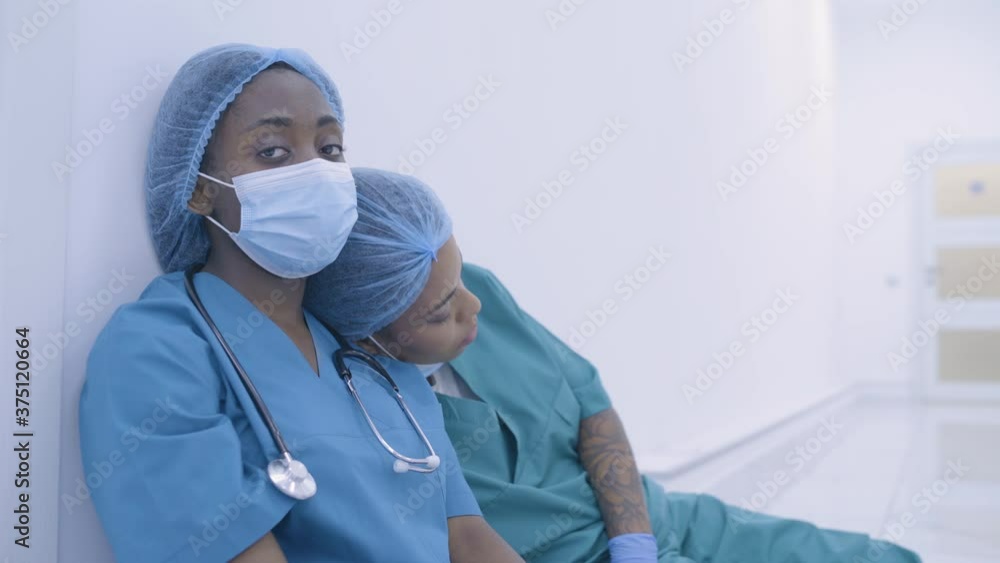 Exhausted young female doctors sitting on floor in hospital, mutual support Exhausted young female doctors sitting on floor in hospital, mutual support