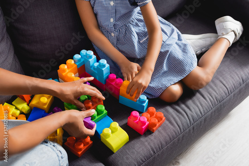 partial view of african american nanny and child playing with multicolored building blocks on sofa