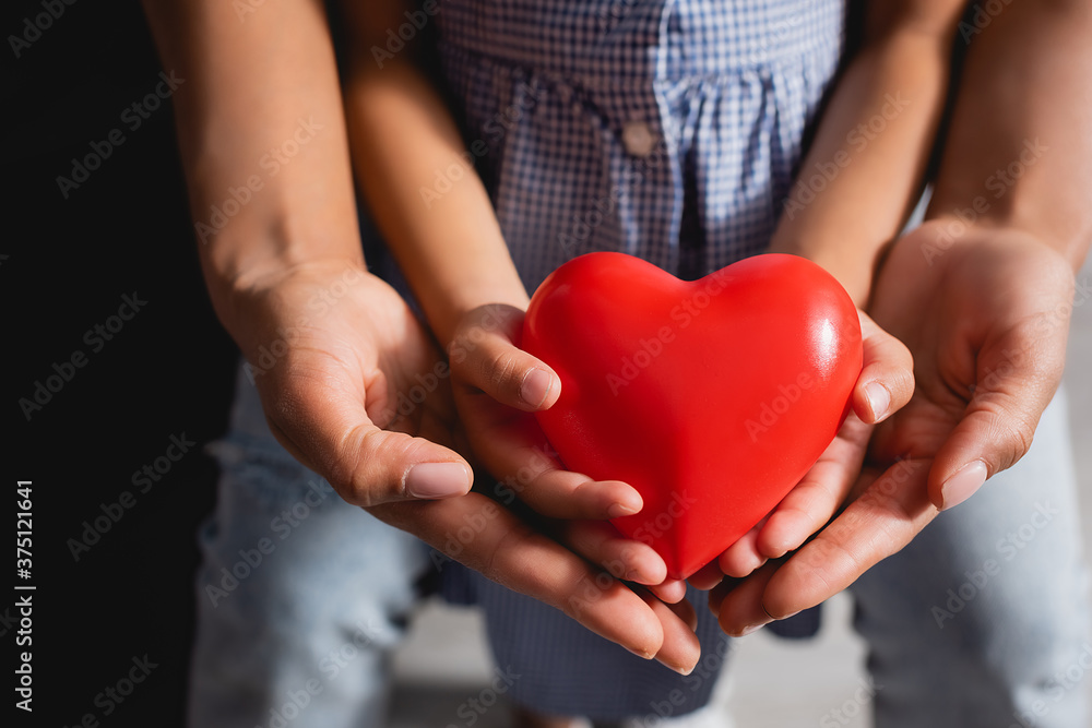 partial view of african american mother and daughter holding red heart model in cupped hands together partial view of african american mother and daughter holding red heart model in cupped hands together