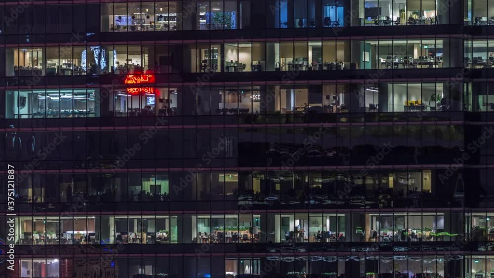 Modern office building with big windows at night timelapse close up view, in windows glowing light shines and some people inside, Singapore. Zoom out Modern office building with big windows at night timelapse close up view, in windows glowing light shines and some people inside, Singapore. Zoom out