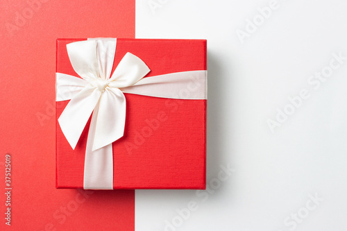 Gift in red box with white ribbon on red and white background, top view