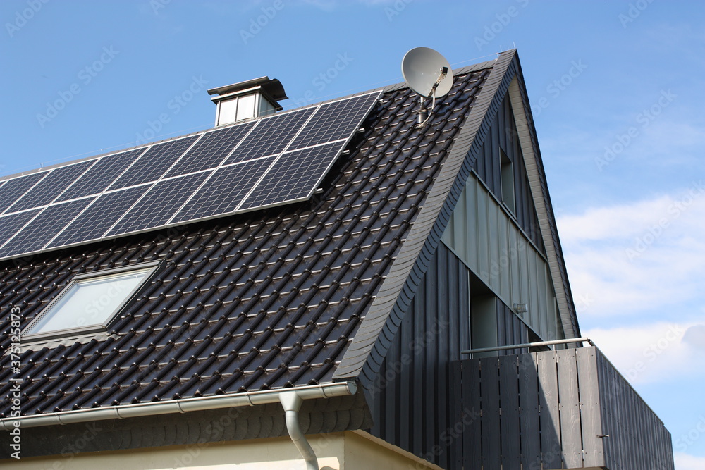 Fototapeta premium Photovoltaikanlage auf einem Haus mit Balkon, Kaminabdeckung und Satellitenschüssel, bei blauem Himmel und Sonnenschein, in Lippetal Büninghausen an der Buschstraße