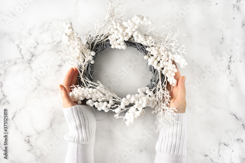 Female hands with white warm sleaves holding a Christmas wreath against marmor background photo