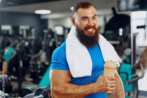 Bearded young man bodybuilder in blue t-shirt standing in gym