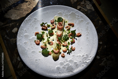 Shripms on asparagus with sauce and garnish on a white plate. photo