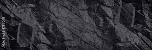 Black stone background. Dark rock texture. Mountain surface texture. Close-up. A wide banner with a volumetric stone texture. Black background with copy space for your design.