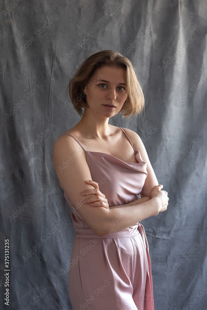 portrait of young caucasian woman with short hair posing in pink suit, standing in front of fabric background. pretty girl in blouse. attractive pensive female poses with arms crossed portrait of young caucasian woman with short hair posing in pink suit, standing in front of fabric background. pretty girl in blouse. attractive pensive female poses with arms crossed