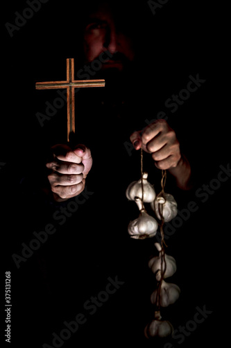 Monk in the dark holding a crucifix and a garlic string, vampire cult and their Fototapet
