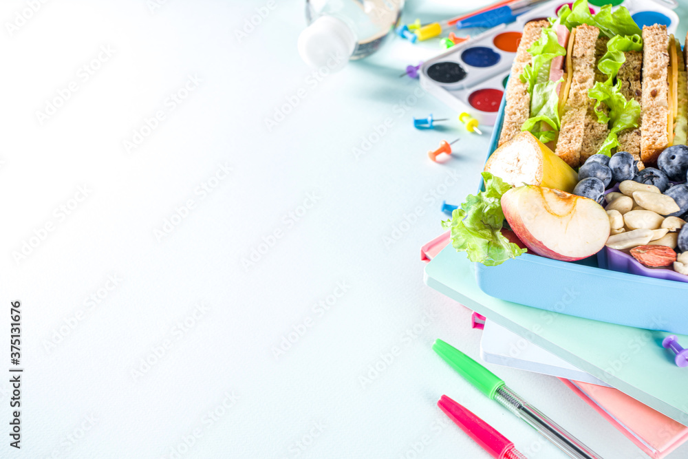 Obraz premium Healthy children school lunch box: sandwich, vegetables ,fruit and mineral water bottle, with school supplies on, on light blue background copy space