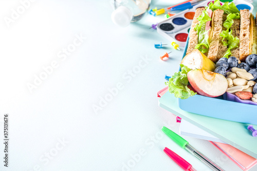 Healthy children school lunch box: sandwich, vegetables ,fruit and mineral water bottle, with school supplies on, on light blue background copy space