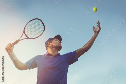 active young man playing tennis outdoors. serve the ball against blue sky
