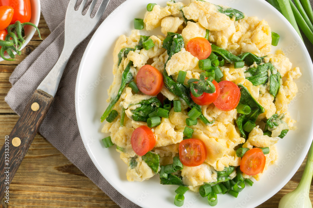 scrambled eggs with spinach and tomatoes on a white plate. scrambled eggs with spinach and tomatoes on a white plate.