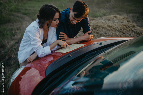 Couple in love looks at guidebook and chooses travel route on hood of car.