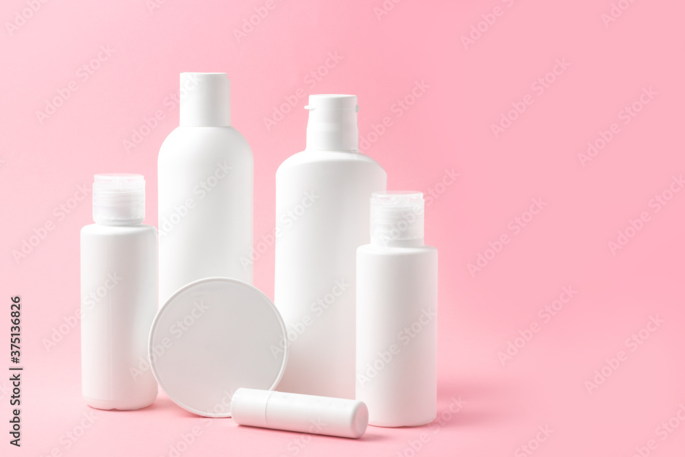 Set of white cosmetic bottles and jars on pink background with place to add text Set of white cosmetic bottles and jars on pink background with place to add text