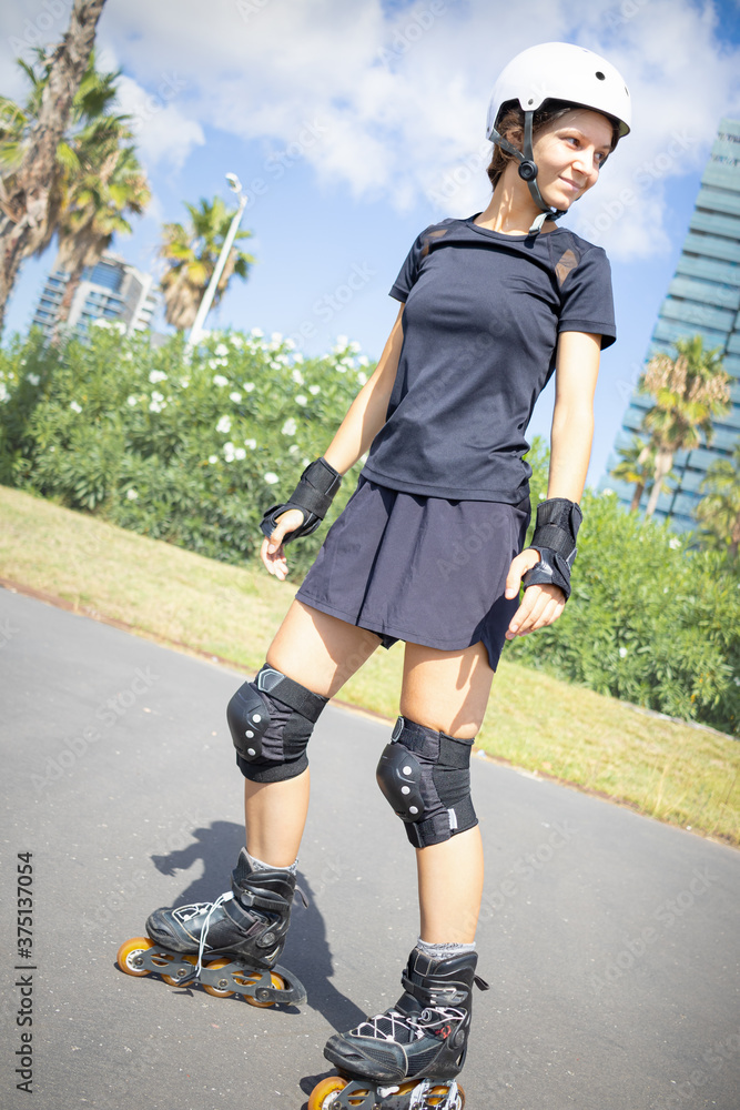 Young happy roller skater caucasian woman in the white helmet and black sporty clothes, sunny day, skatepark, urban environment. Young happy roller skater caucasian woman in the white helmet and black sporty clothes, sunny day, skatepark, urban environment.