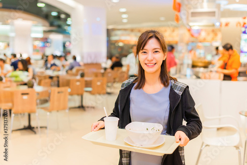 Asian businesswoman eat food at food court and blurry food court at supermarket/mall for background with bokeh. Female having lunch at food court.