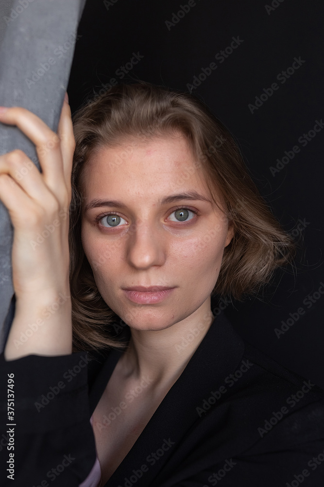 Obraz premium portrait of young caucasian woman with short hair posing in black suit jacket, holding curtain. closeup shot of pretty girl. short-haired attractive female poses in studio