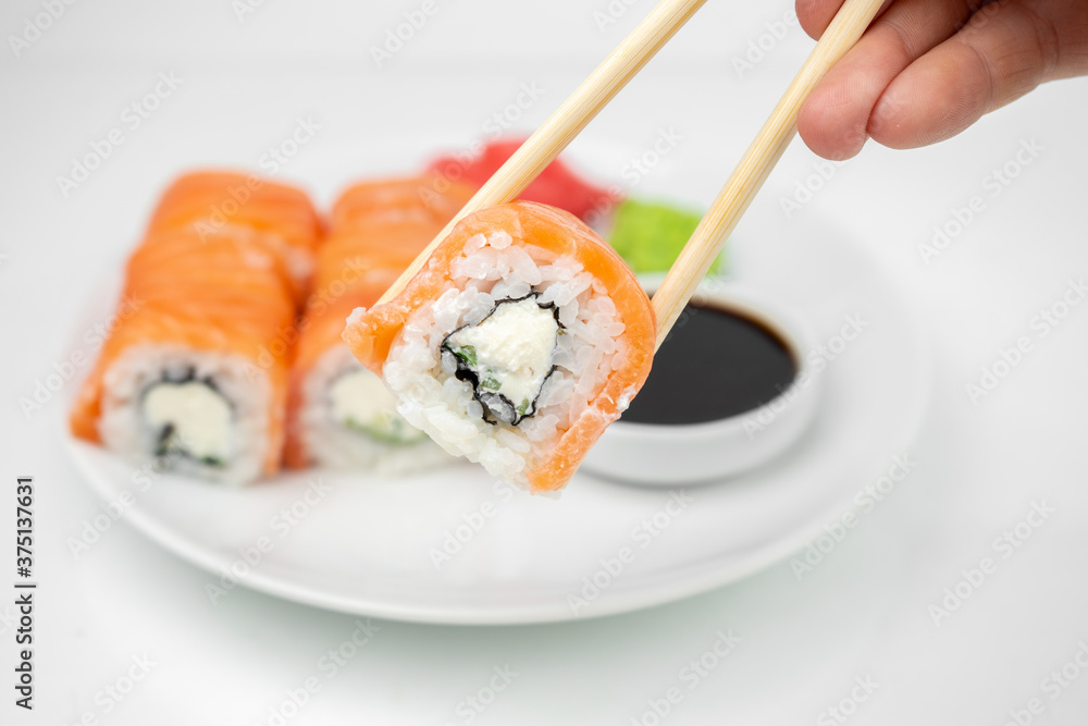 take a philadelphia maki rolls with bamboo chopsticks and put in into  soy sauce. pink ginger, wasabi on white plate, asian food, japanese cuisine background
