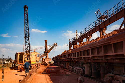 Aluminium ore (Bauxite clay) mining and processing plant. Load and railway transporting terminal and hopper car. Workers (left).