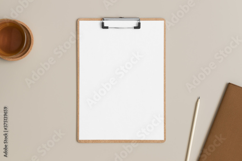 Wooden clipboard mockup with a cup of tea and workspace accessories on a beige table.