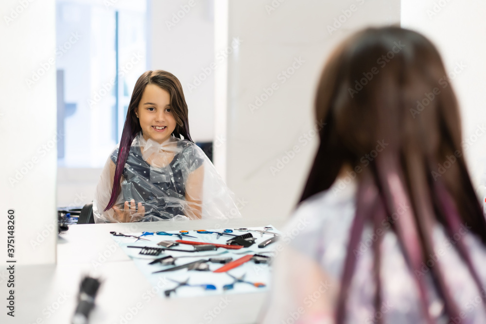 Fototapeta premium little girl dyes her hair purple in a hairdressing salon