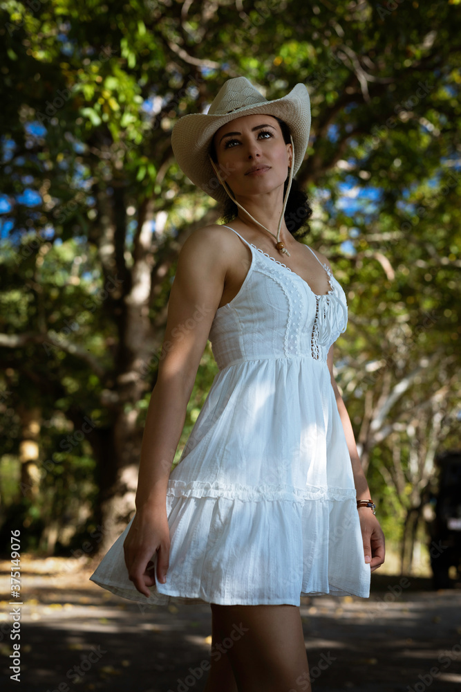 A beautiful young curly-hair woman in a little white/beige dress is posing in the forest. Portrait Photography.
